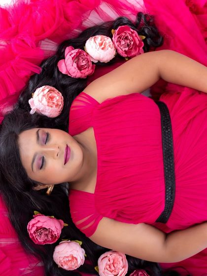 An artistic overhead shot of a mom-to-be in a pink dress, lying down with flowers scattered in her hair.
