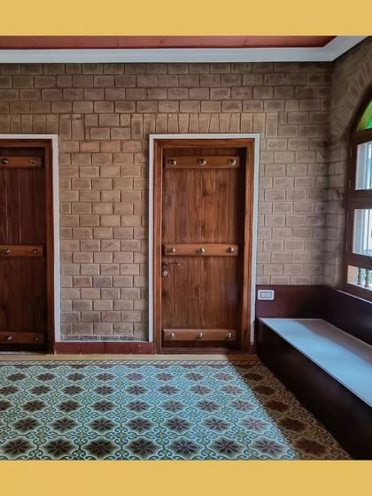 An interior with patterned Athangudi floor tiles, traditional wooden doors, and exposed soil cement block walls.