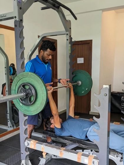 Assessment week is crucial for program design. Here, an athlete performs a bench press under the watchful eye of a strength coach to establish baseline strength levels.