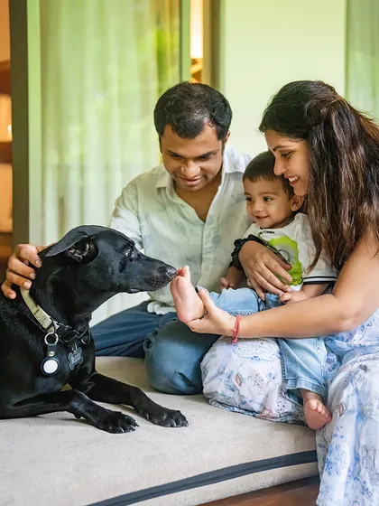 The whole family together, focused on the connection. Rio the dog gently sniffs baby Vyom's foot, held by his loving parents. It's these small, tender gestures that make for the most memorable family and pet photographs.