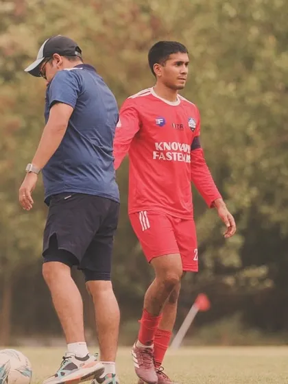 A player focused on the ball while the coach observes his technique. This highlights the individual attention given during our professional football training sessions.