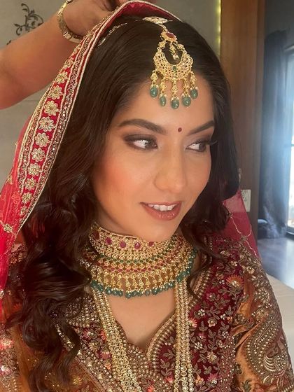 A beautiful bride ready for her Pheras. The makeup features a classic smokey eye and a warm lip color to complement her traditional red and gold attire.