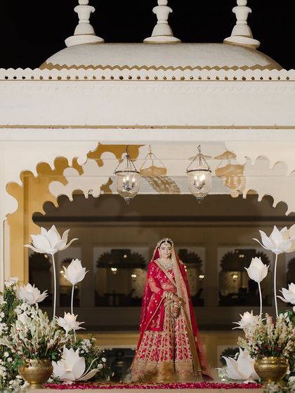 A grand bridal entry. The bride looks majestic in her red Sabyasachi lehenga, with minimal makeup and a sleek hairstyle that exudes regal elegance.