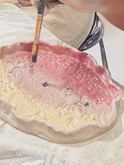 A student applies a colorful gradient of underglaze to their textured plate, creating a beautiful ombre effect.