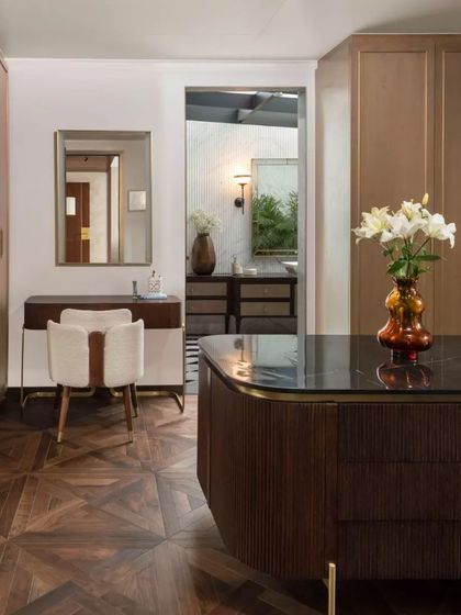 Another view of the dressing area, showing the seamless integration of the vanity, closet, and a glimpse into the en-suite bathroom. The material palette of wood, brass, and stone is consistent throughout.