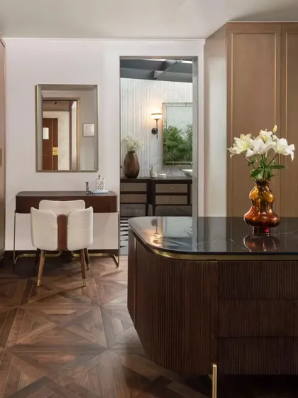 Another view of the dressing area, showing the seamless integration of the vanity, closet, and a glimpse into the en-suite bathroom. The material palette of wood, brass, and stone is consistent throughout.