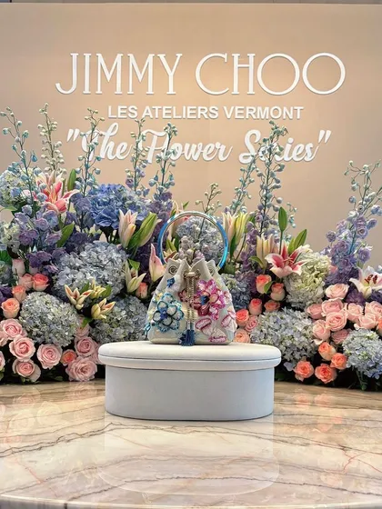 A product display designed for the launch of Jimmy Choo's 'The Flower Series'. The new handbag is presented on a pedestal, framed by an exquisite arrangement of pastel hydrangeas, roses, and lilies, perfectly reflecting the collection's floral elegance.
