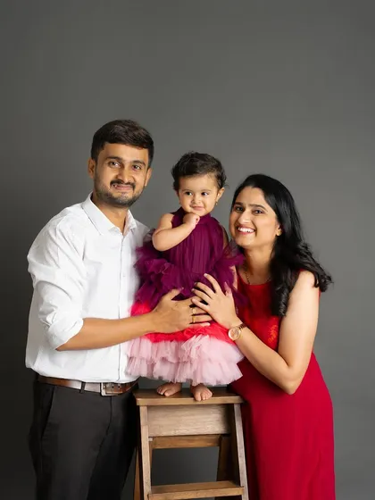 A happy family of three in a classic studio setting. The daughter's colorful dress stands out beautifully against the parents' simpler outfits.