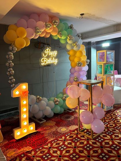 A soft and dreamy pastel balloon ring for a first birthday. This decoration uses a beautiful palette of pastel colors, a light-up number '1', and custom name blocks to create a personalized and whimsical photo area.