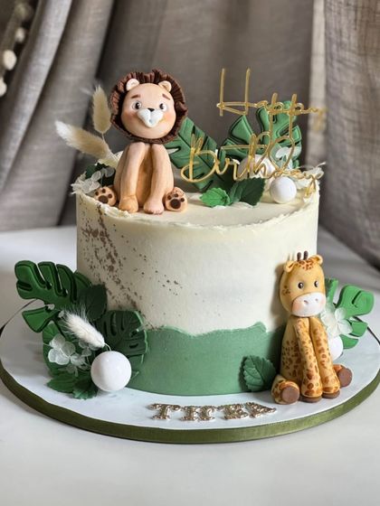 Wild ONE vibes are activated with this jungle-themed birthday cake. It features handcrafted edible toppers like a lion and giraffe, soft greenery, and fun safari feels.