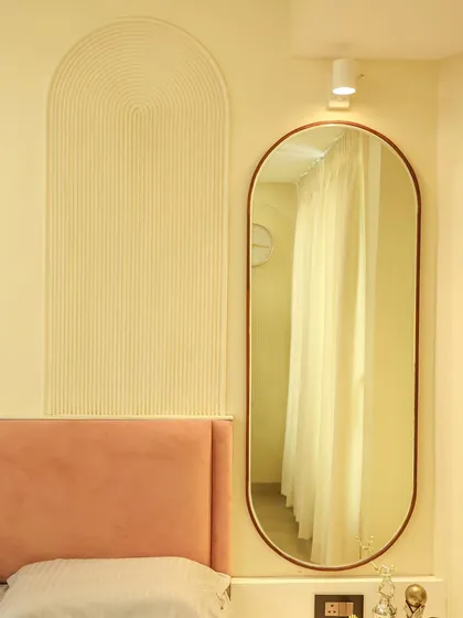 The arched fluted panel beside the bed adds a textural element that complements the soft curves of the headboard and oval mirror.
