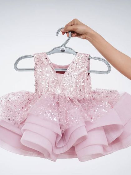 This sparkling pink baby frock is perfect for a birthday party. It features a sequined top and a layered tulle skirt, available to either rent or buy.
