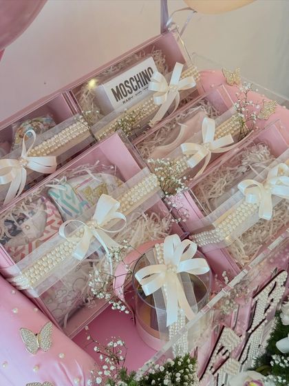 A peek inside the acrylic boxes, revealing beautifully wrapped gifts including a Moschino baby item, all tied with satin bows.