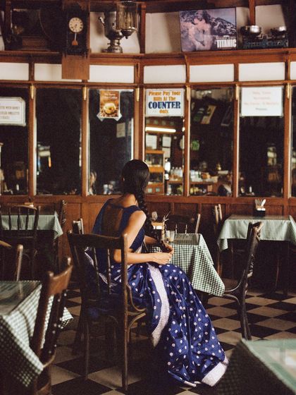 A quiet moment of solitude in a classic Irani cafe. The setting provides a rich, textured backdrop for the simple elegance of the polka-dotted Banarasi saree.