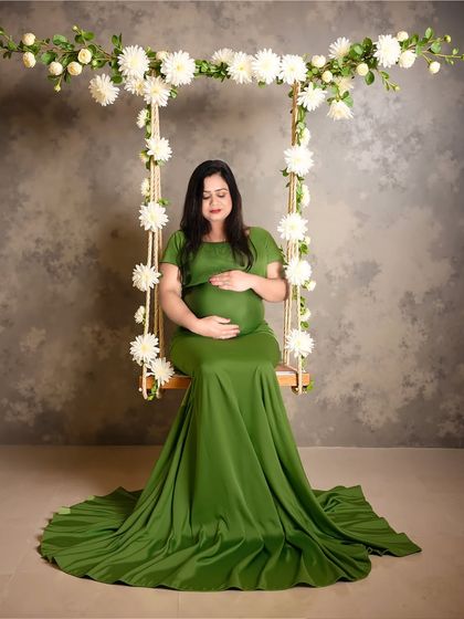 A simple and elegant studio portrait on a floral swing. The focus is on the mom-to-be's serene expression as she cradles her bump.