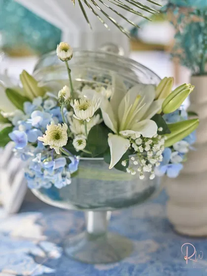 A beautiful arrangement of white lilies and blue hydrangeas in a glass compote, capturing the fresh, elegant feel of the event.