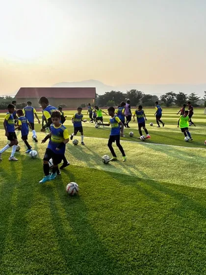 A wide shot of numerous players engaged in ball mastery drills across the pitch. This image shows the scale and intensity of the training provided at our camps.