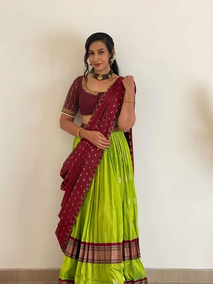A classic langa voni or half saree in a vibrant lime green and maroon combination. This traditional outfit is perfect for festivals and family functions, designed to be both beautiful and comfortable. The blouse features delicate handwork on the sleeves.