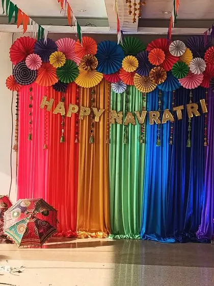 A colorful and joyous backdrop for a Navratri celebration. I used rainbow-colored drapes, paper fan decorations, and traditional umbrellas to create a lively and energetic atmosphere perfect for garba and festivities.