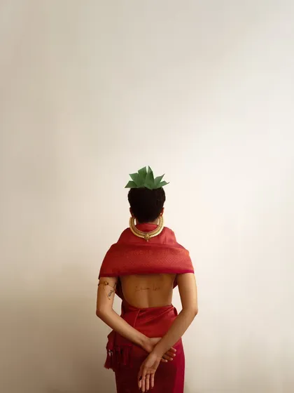 A minimalist back shot that highlights the details of the hairstyle, the gold neckpiece, and the model's tattoo. The negative space in the composition creates a quiet, contemplative mood.