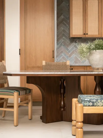 The dining area in our 'Kolam Pop' home features a table with a sculptural wooden base and lathe-turned accents. It's paired with woven chairs and a patterned bench, celebrating artisanal heritage with a modern twist.