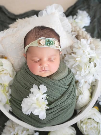 A beautiful close-up of a baby girl wrapped in olive green, surrounded by white flowers. The contrast is both earthy and elegant.