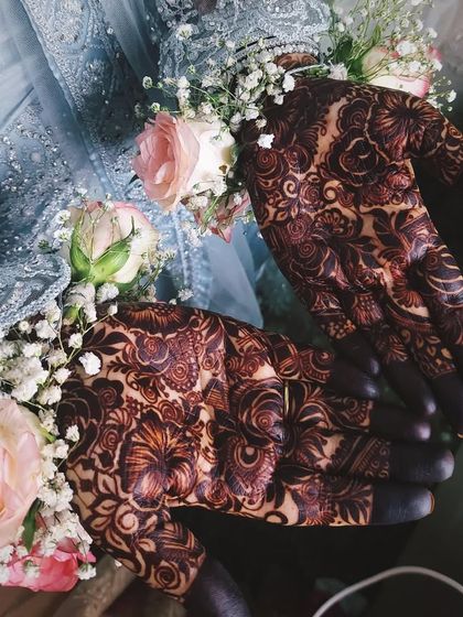 A stunning bridal portrait showcasing the dark, elegant stain of the mehendi, perfectly complemented by floral bracelets and a beautiful gown.