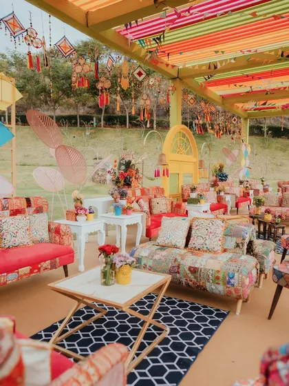 A vibrant and eclectic lounge for a Kite Carnival event, featuring patchwork sofas, colorful overhead drapes, and hanging traditional crafts that create a festive and bohemian atmosphere.