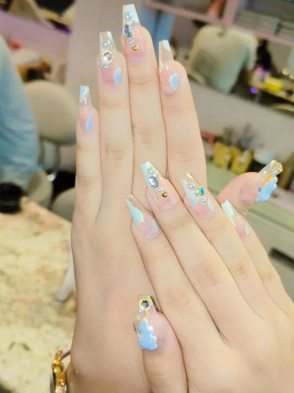 Long, clear coffin nails with a touch of light blue, adorned with rhinestones and 3D floral accents. This is a delicate and intricate design for a standout look.