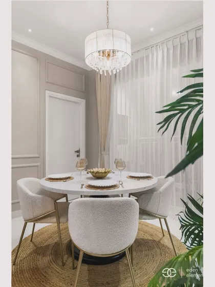 A wider view of the dining area, showing the round jute rug that anchors the space. The large plant adds a touch of nature, balancing the modern and classic elements of the room.