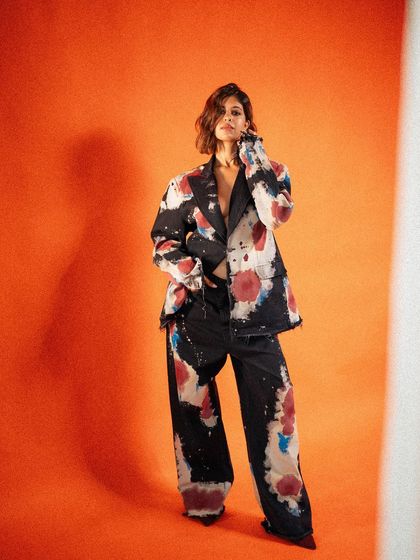 A full-length shot of a hand-painted suit from Huemn against a bold orange background, creating a vibrant, art-focused fashion statement.