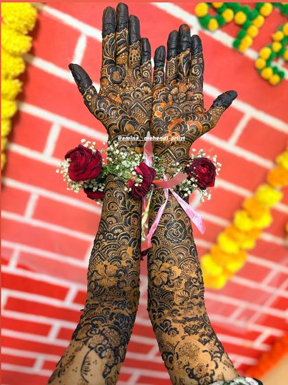 The combination of intricate henna, floral jewelry, and a colorful background makes for a perfect mehendi ceremony photo.