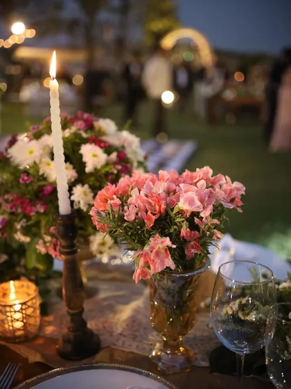 The magic of candlelight. This close-up captures the romantic ambiance of an evening event, with a single candle illuminating a delicate bouquet of pink flowers.