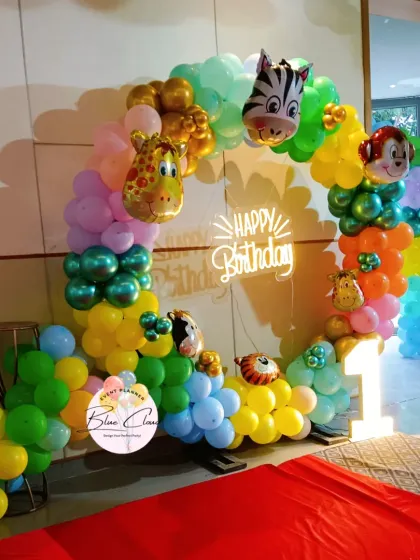 A vibrant jungle-themed balloon ring for a first birthday, featuring animal foils, a neon sign, and a light-up number '1'.