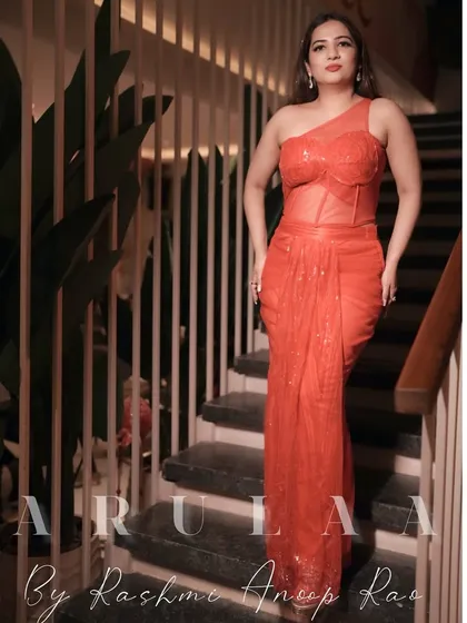 Another view of the red-orange draped saree. The one-shoulder design and sheer corset panel add a modern and glamorous touch.