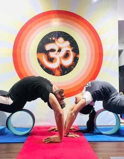 A partner pose using the yoga wheel to support a deep backbend. This is a wonderful way to open the spine while connecting with a fellow practitioner.