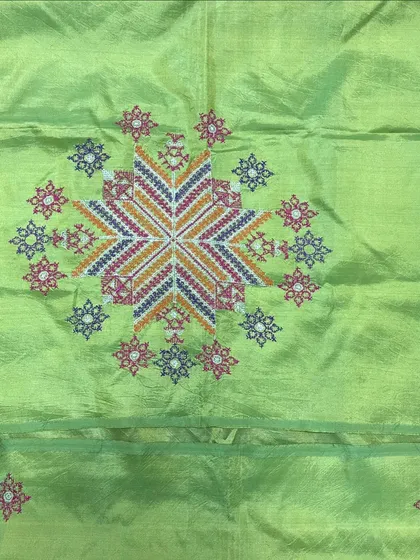 A beautiful light green Tussar silk saree featuring a large, intricate star-shaped Kasuti motif. The multi-colored threads create a stunning focal point.