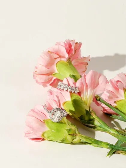 Diamond rings are gently placed among soft pink carnations, creating a romantic and delicate visual. This shot is perfect for showcasing bridal or special occasion jewellery.