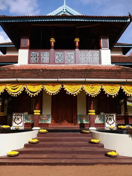 Decorating a 75-year-old heritage home in Kerala, with traditional marigold garlands accentuating the beautiful architecture under a clear blue sky.