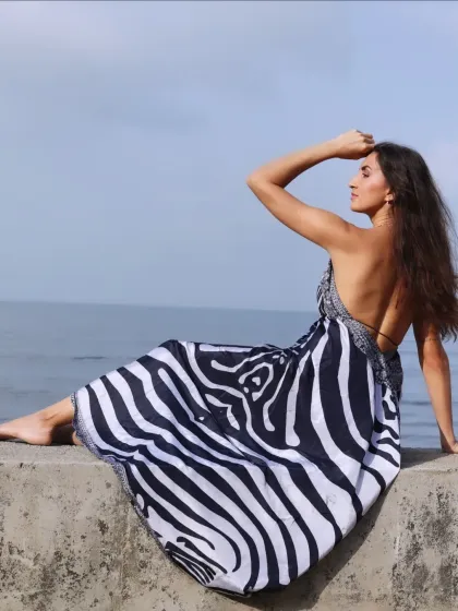 A relaxed portrait of a model sitting on a sea wall, looking out at the ocean.