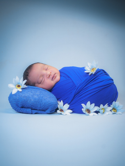 A full view of the wrapped newborn on a blue backdrop. The swaddling technique keeps the baby secure and comfortable, which helps create these peaceful portraits.