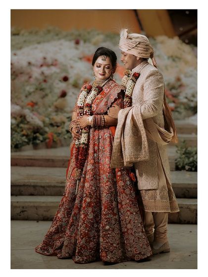 A beautiful full-length portrait of the couple against a backdrop of flowers, showcasing their elegant wedding attire.