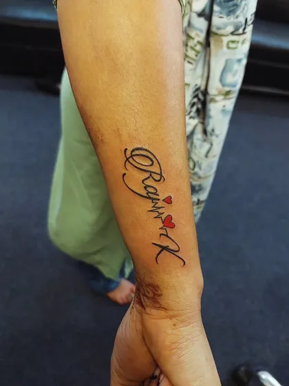 A name tattoo that incorporates a heartbeat line and red hearts. This design adds a dynamic and personal touch to a classic script tattoo.