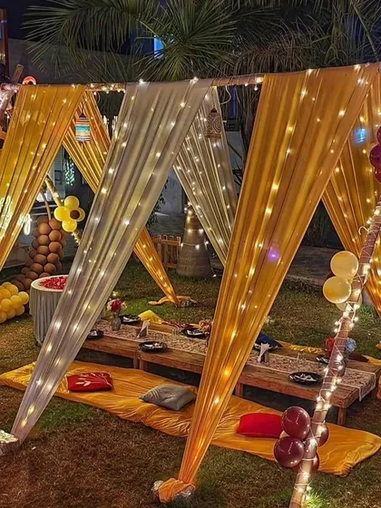 An elegant canopy created with yellow and white drapes and fairy lights, providing a beautiful covered dining area for an outdoor event.