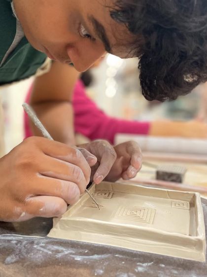 A student meticulously carves details into a rectangular tray, demonstrating the architectural possibilities of slab building.