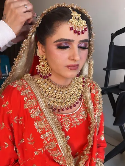 A close-up of an Anand Karaj bride during her getting ready process. The glittery purple smokey eye adds a touch of drama to her traditional red and gold outfit.