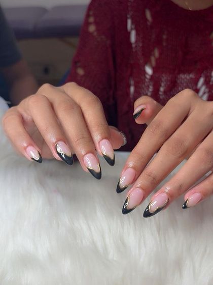 A modern twist on the French manicure with sharp, V-shaped black tips and a delicate gold chrome line. This edgy design on long almond extensions is perfect for making a statement.