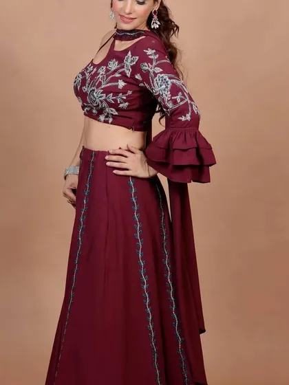 A side view of the maroon Indo-Western lehenga, showing the beautiful floral embroidery and the unique one-sleeve design with a ruffled cuff. It's a perfect blend of traditional motifs and contemporary style.