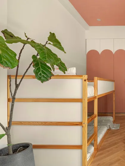 A closer view of the bunk bed and the custom wardrobe. The gentle curve of the blush-pink wardrobe doors softens the room's geometry, while the natural wood of the bed frame adds warmth and texture.