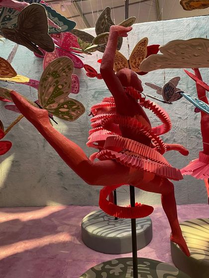 A close-up of a dancing figure from the 'We/Us' installation, surrounded by butterflies. The piece is a bold and confident statement on ungendering spaces, using fashion and movement as its primary language.